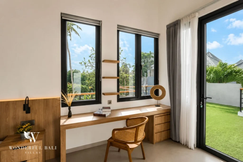 A bedroom study corner with a built-in timber desk, rattan chair and windows framing the garden at a 4-bedroom villa in Pererenan, Bali
