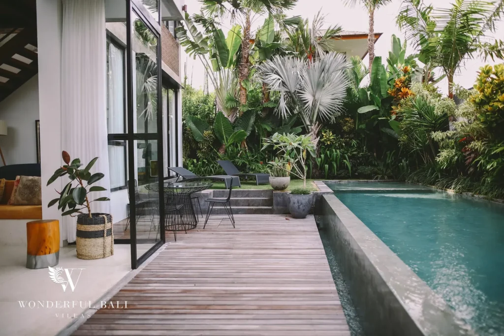 A timber pool deck running alongside the private pool with an outdoor dining set and dense tropical planting at a 4-bedroom villa in Batu Bolong, Canggu, Bali