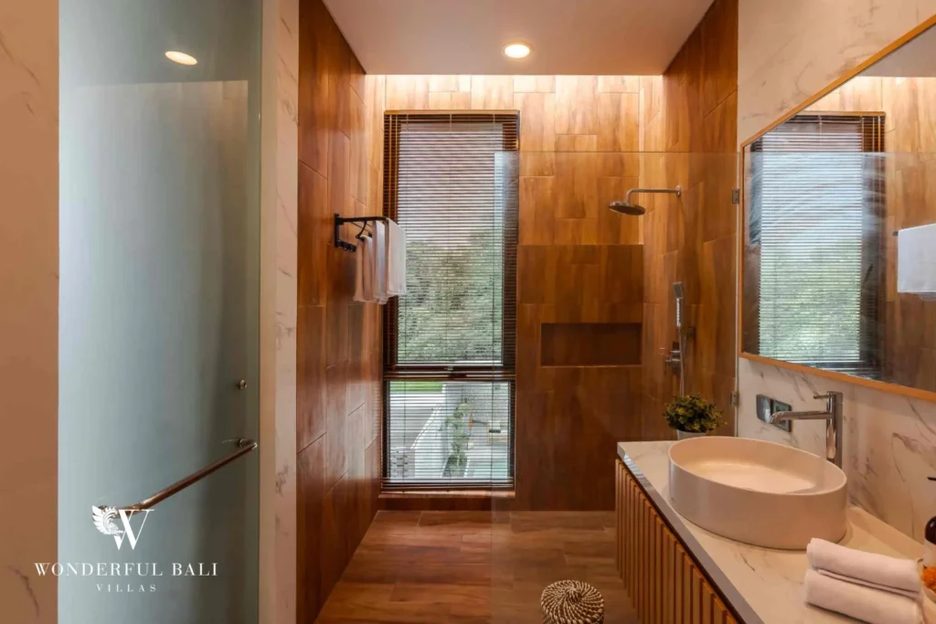 A warm timber-clad ensuite with a walk-in rain shower, stone vessel sink and garden-view window at a 4-bedroom villa in Pererenan, Bali