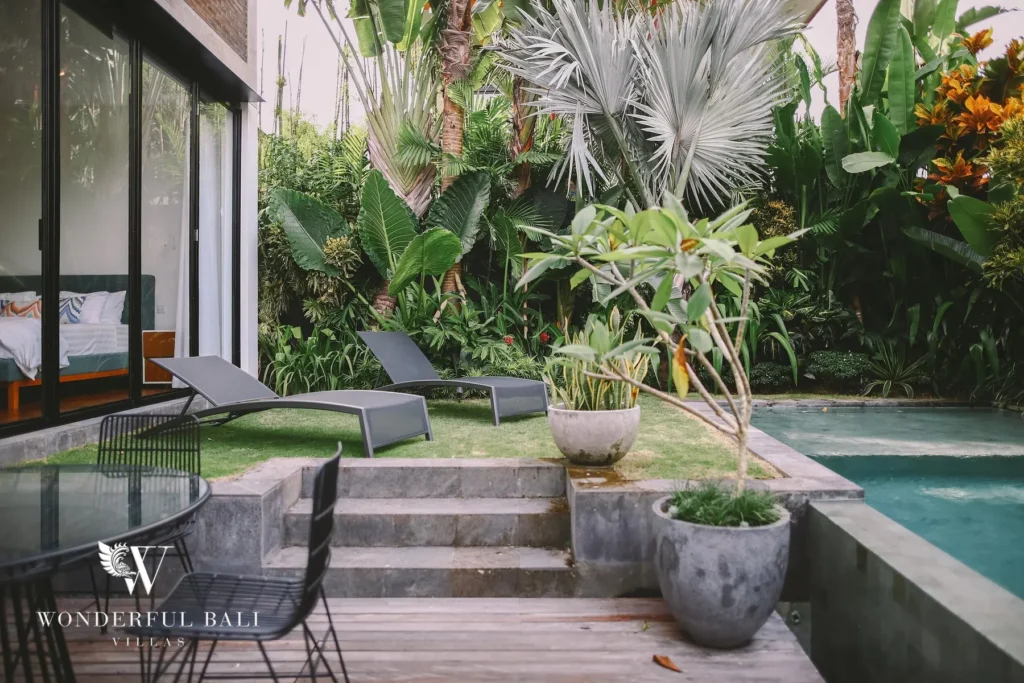 A garden terrace with sun loungers on a lawn beside the pool, framed by palms and lush greenery at a 4-bedroom villa in Batu Bolong, Canggu, Bali