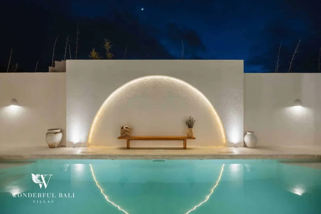 The pool lit at night beneath a crescent moon, with an illuminated arched wall and a wooden bench, at a 2-bedroom villa in Bingin, Uluwatu, Bali