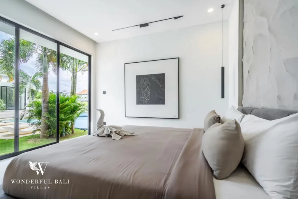 King bedroom with a taupe bed and framed artwork beside glass doors to the pool and garden at a 5-bedroom villa in Pererenan, Bali
