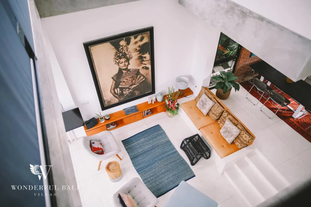 An elevated view down into the living room showing a large framed portrait, leather sofa and blue rug at a 4-bedroom villa in Batu Bolong, Canggu, Bali