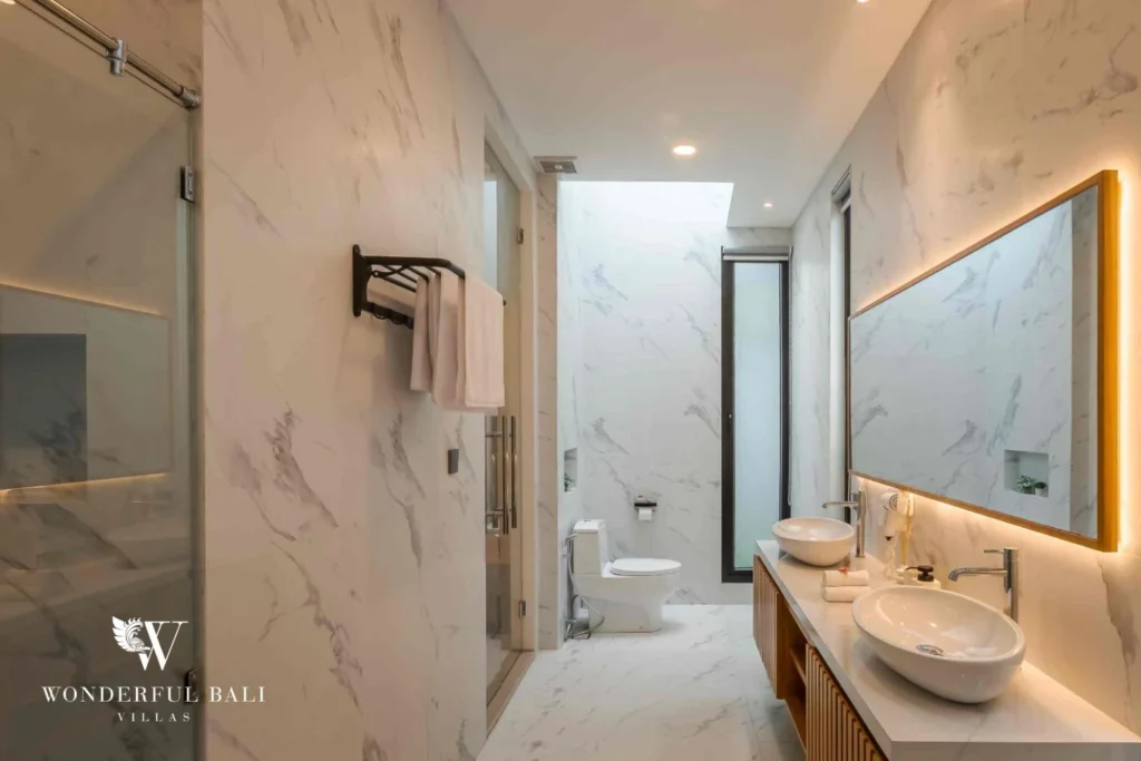 A marble ensuite with double vessel sinks, a walk-in shower and a separate toilet at a 4-bedroom villa in Pererenan, Bali