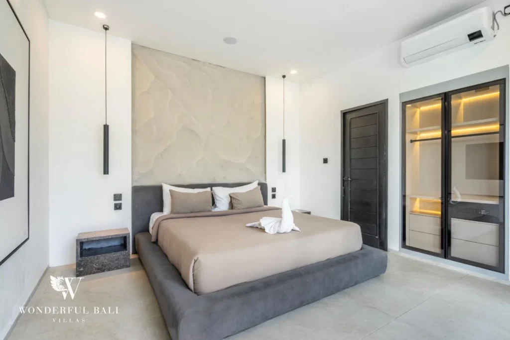 King bedroom with a textured feature wall, dark wooden door and glass-fronted walk-in wardrobe at a 5-bedroom villa in Pererenan, Bali