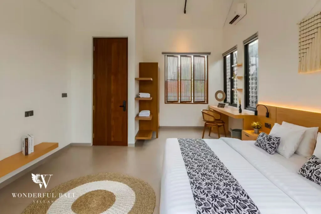 A king bedroom with timber door, built-in shelving and a desk nook beside slatted windows at a 4-bedroom villa in Pererenan, Bali