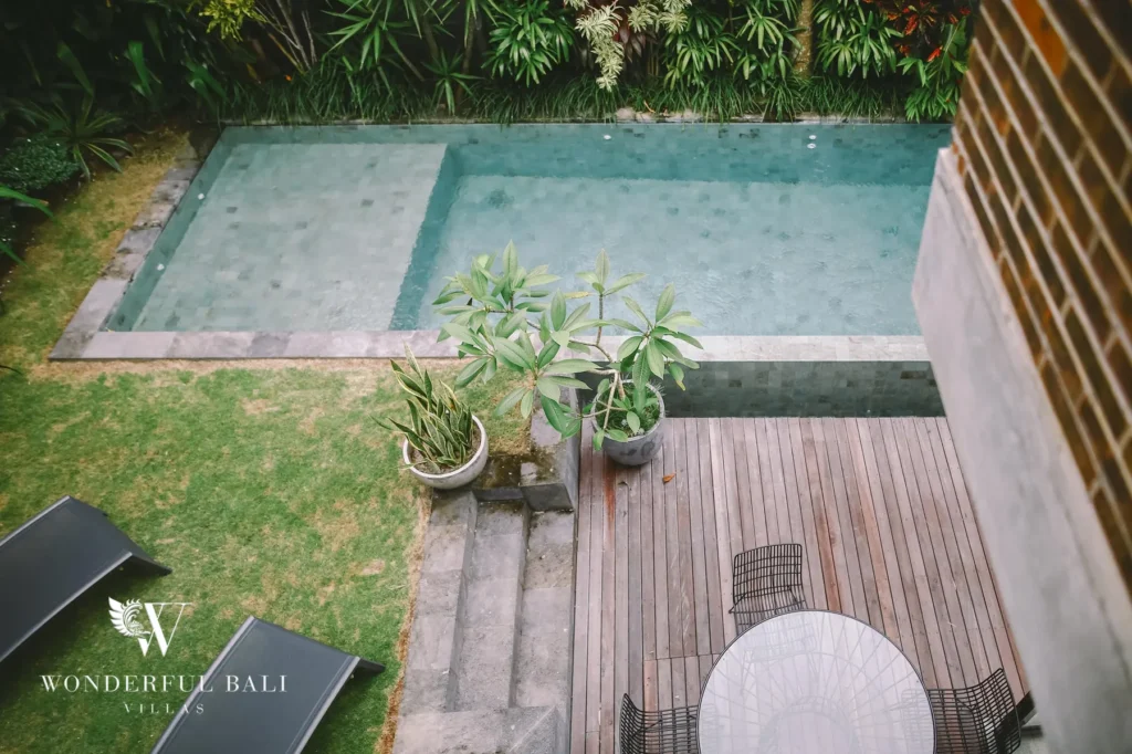 An aerial view of the private pool, timber deck, lawn with sun loungers and surrounding tropical garden at a 4-bedroom villa in Batu Bolong, Canggu, Bali