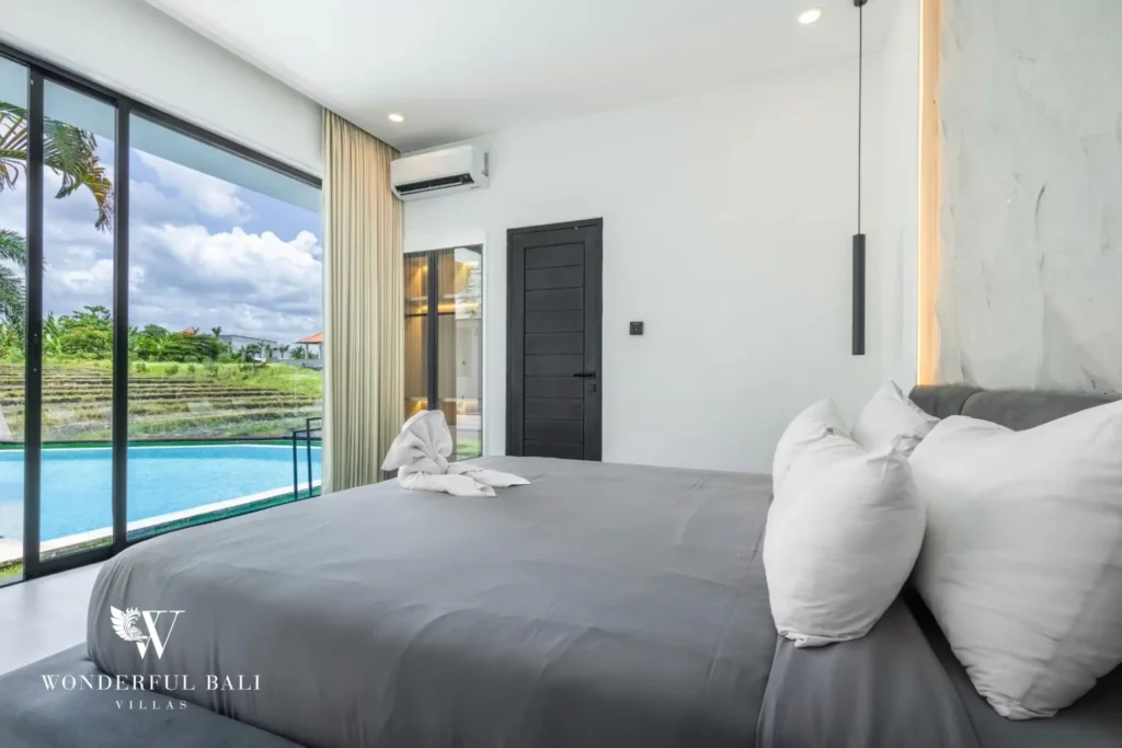 King bedroom with a grey bed and glass doors framing views of the pool and rice fields at a 5-bedroom villa in Pererenan, Bali