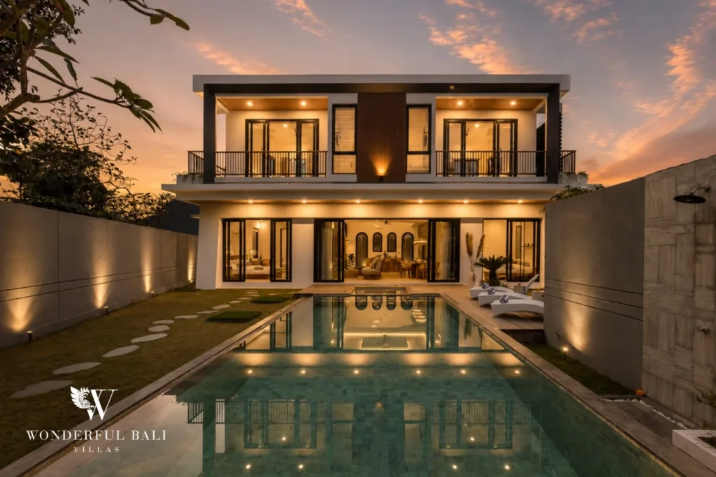 The illuminated villa facade at dusk reflected in the pool with a glowing double-height living room at a 4-bedroom villa in Pererenan, Bali