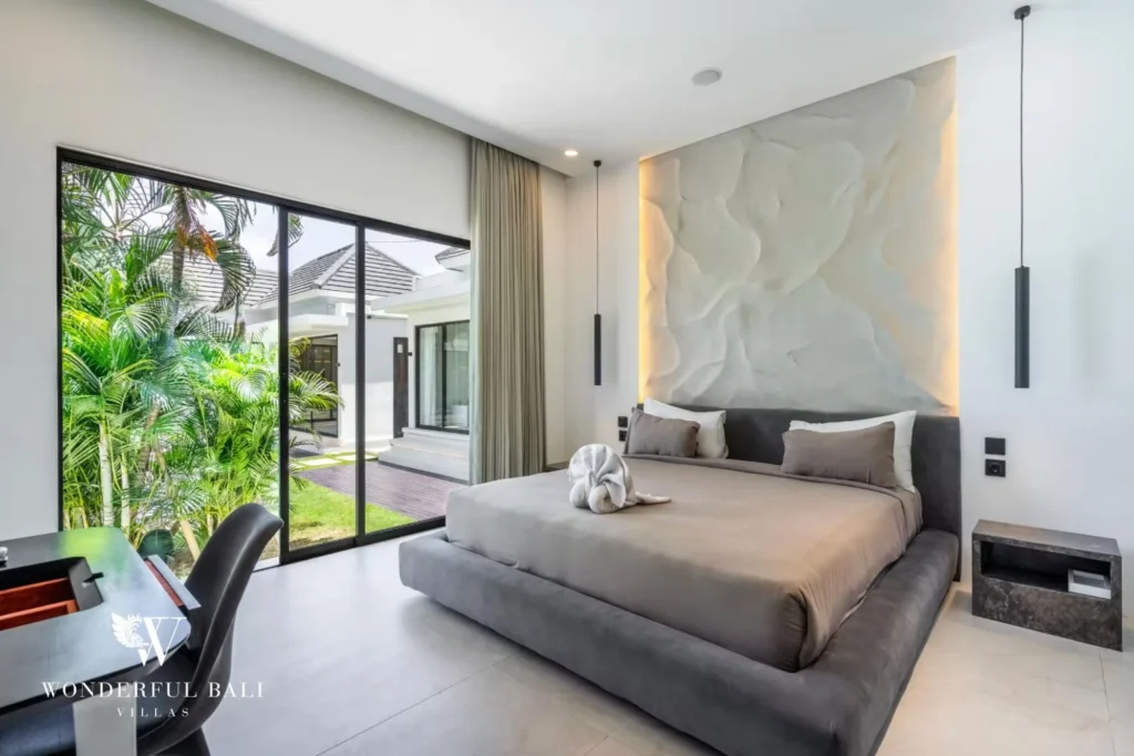 King bedroom with a sculpted headboard, writing desk and glass doors to the tropical garden at a 5-bedroom villa in Pererenan, Bali
