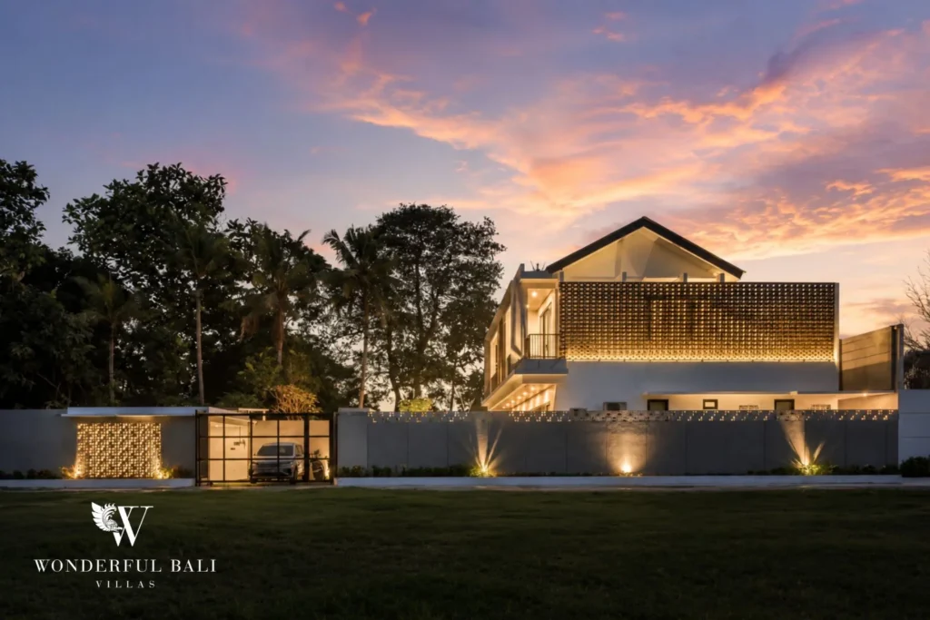 A dusk street view of the illuminated villa behind its lit perimeter wall with palms and a parked car at a 4-bedroom villa in Pererenan, Bali