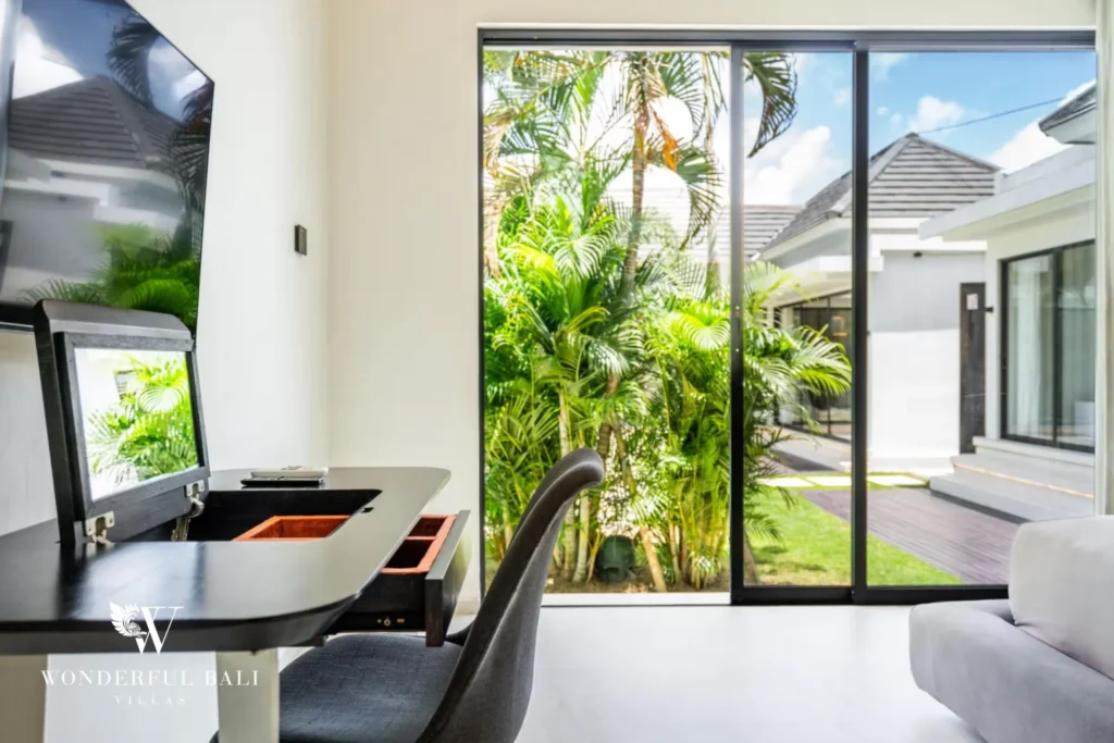Bedroom workspace with a dark desk and chair beside glass doors opening to the palm garden at a 5-bedroom villa in Pererenan, Bali