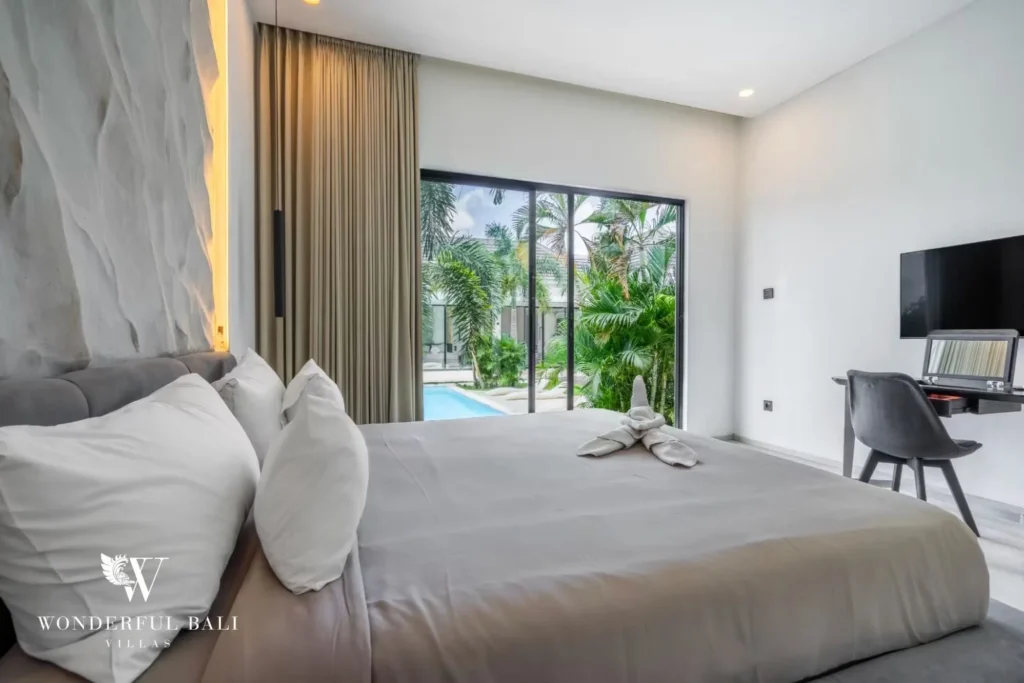 King bedroom with a grey bed, desk and glass doors framing the pool and garden at a 5-bedroom villa in Pererenan, Bali