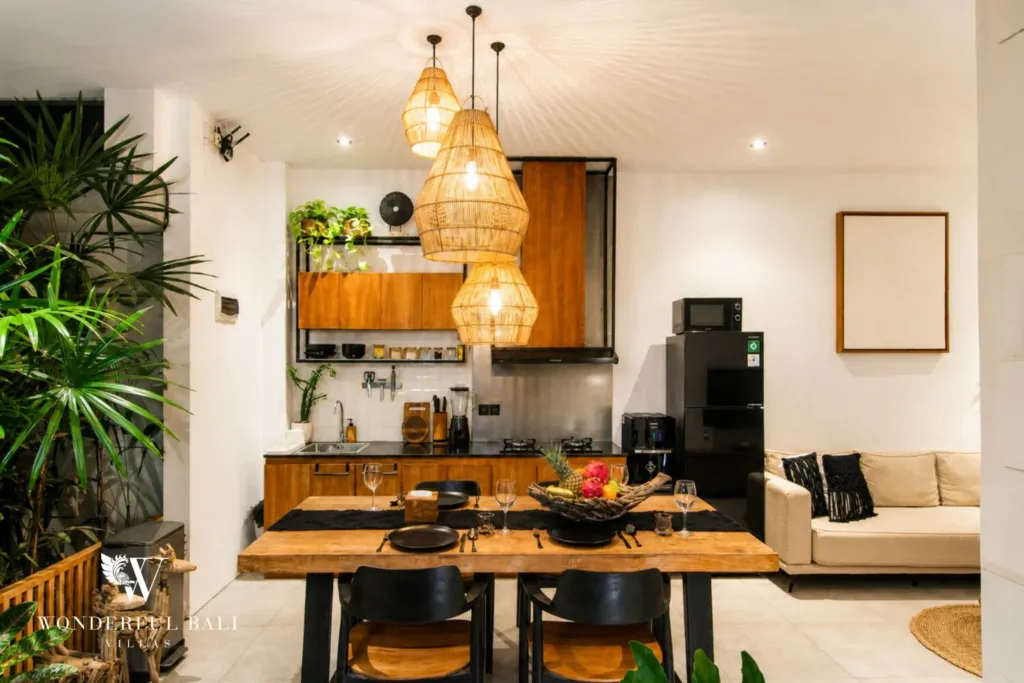 2BR villa for rent in Bumbak, Umalas — kitchen, open-plan timber kitchen and live-edge dining table under three rattan pendants in a 2-bedroom villa