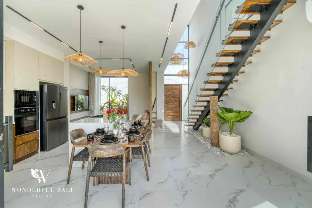 Dining table and open kitchen below a floating timber stair in a 3-bedroom villa near Nusa Dua Bali