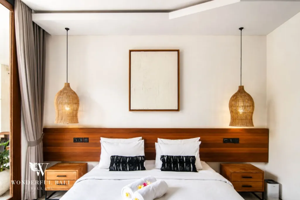 2BR villa for rent in Bumbak, Umalas — bedroom, king bed against a full-width timber headboard under two rattan pendants in a 2-bedroom villa