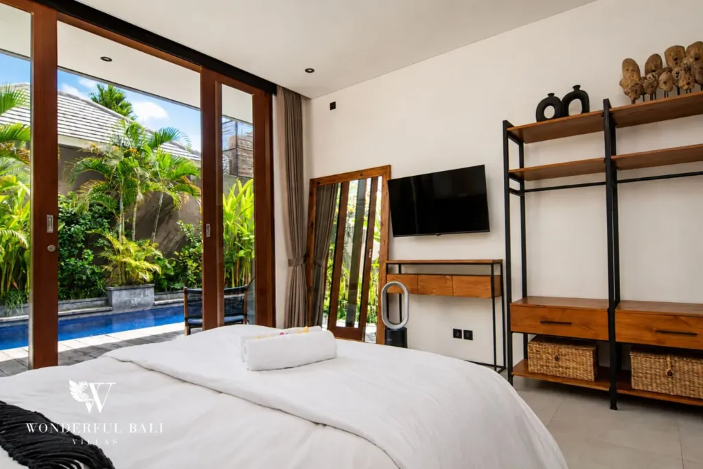 2BR villa for rent in Bumbak, Umalas — bedroom, a smart TV and open shelving beside sliding doors to the pool in a 2-bedroom villa