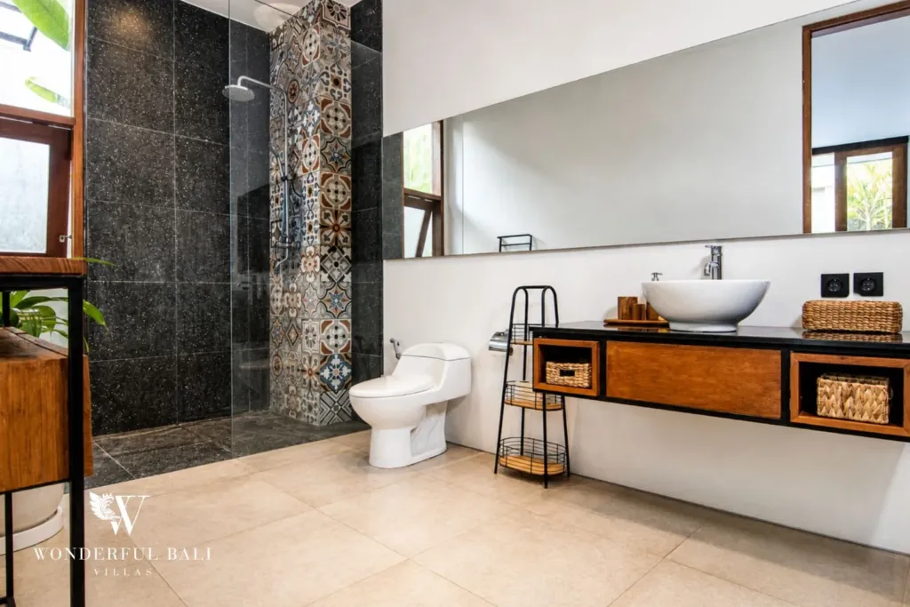 2BR villa for rent in Bumbak, Umalas — bathroom, a long mirror, timber vanity and black stone walk-in shower in a 2-bedroom villa