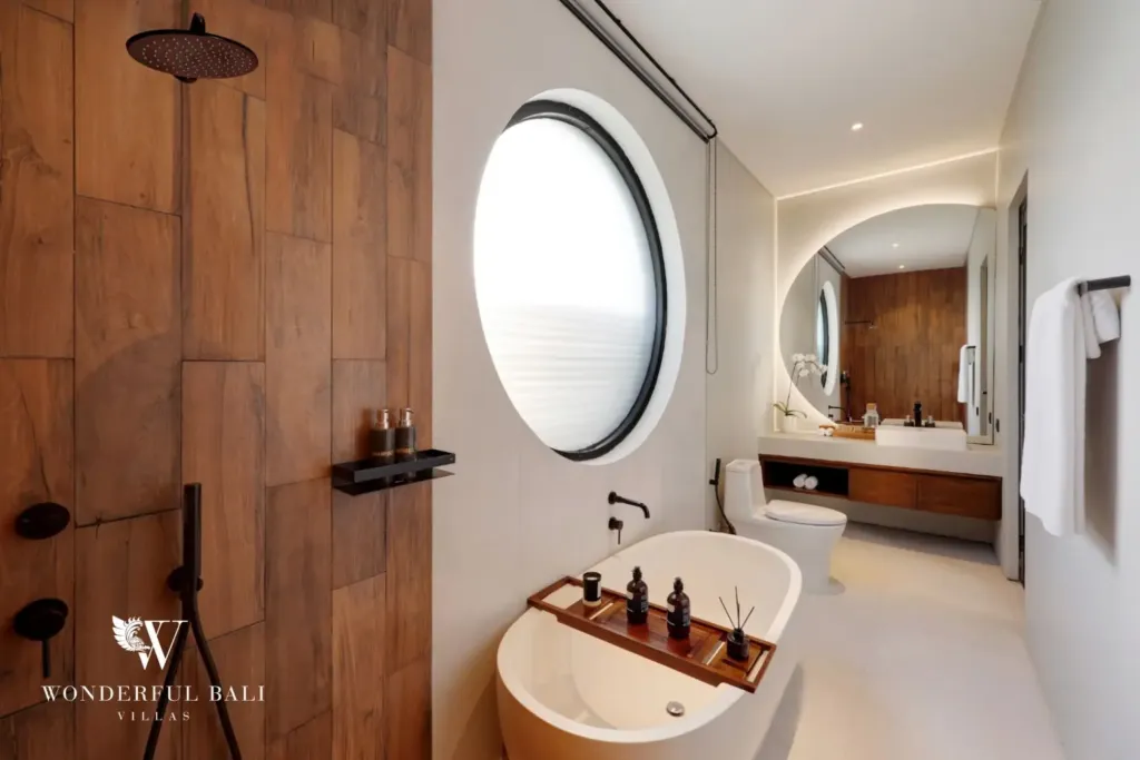 En-suite bathroom with freestanding bathtub and round window at a 3BR villa in Pererenan Bali