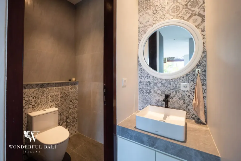 4BR villa for rent in Seminyak — powder room, patterned tile and a round mirror off the hallway