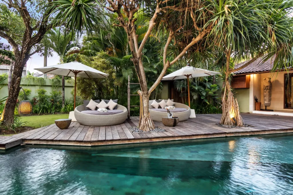 Daybeds and parasols on the deck between the pool and the lawn at Villa Shantika