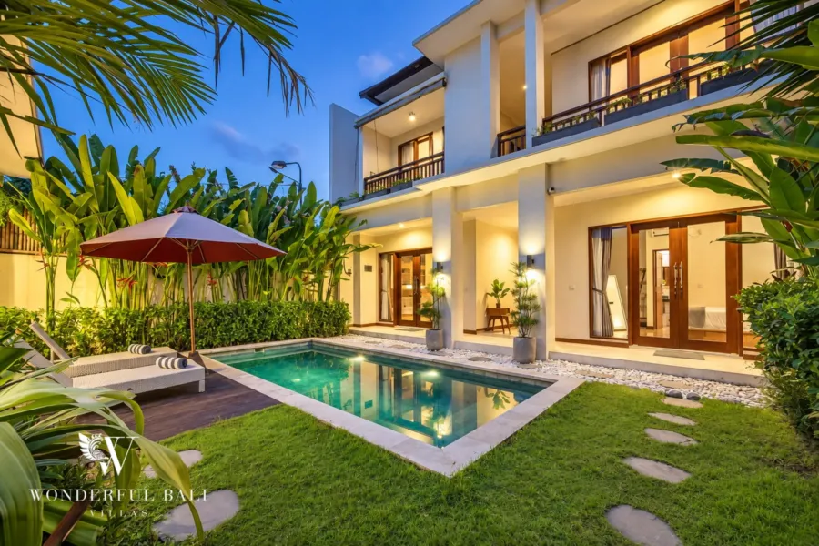 4BR villa for rent in Umalas, Bali — exterior, two-storey villa lit at dusk above the pool, timber deck and lawn