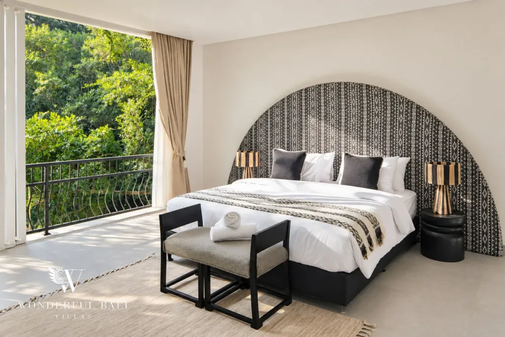 5BR villa for rent in Munggu, Bali — bedroom, king bed under an arched patterned headboard beside a garden balcony