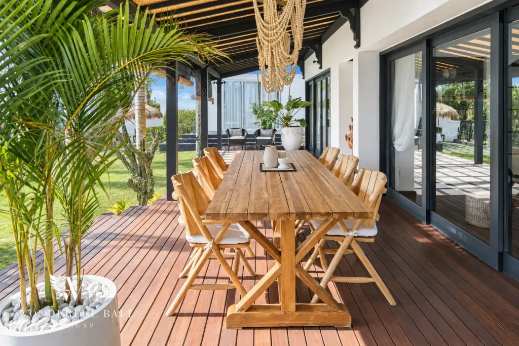 5BR villa for rent in Munggu, Bali — dining area, dining table on the timber deck framed by palms and garden