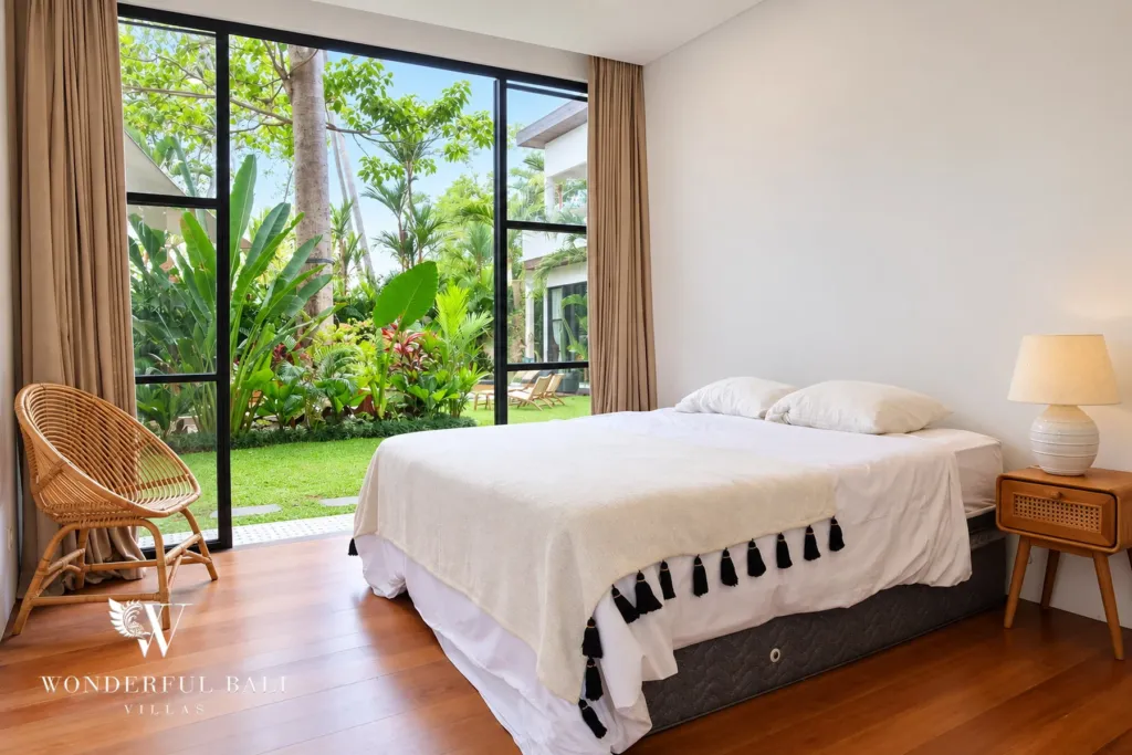 5BR villa for rent in Seseh, Bali — bedroom, bedroom with full-height glass onto the garden and a rattan chair