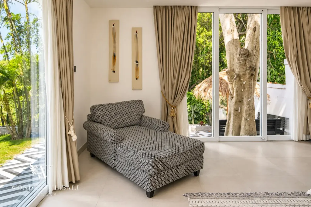 5BR villa for rent in Munggu, Bali — bedroom, upholstered chaise by the window looking into the trees