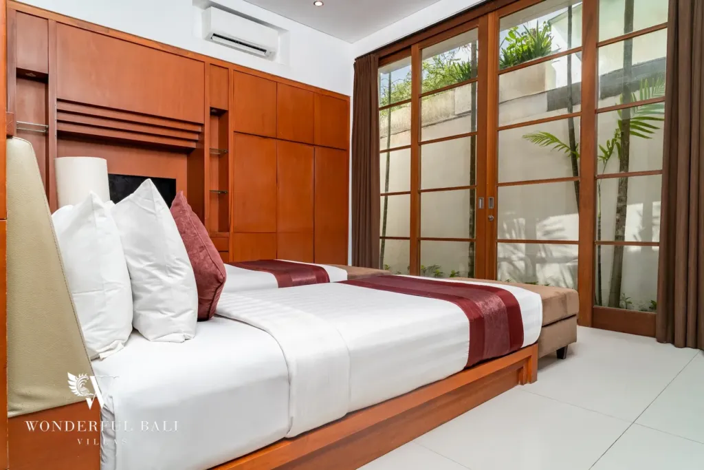 3BR villa for rent in Batu Belig, Seminyak — bedroom, twin beds beside floor-to-ceiling timber-framed glass to the garden