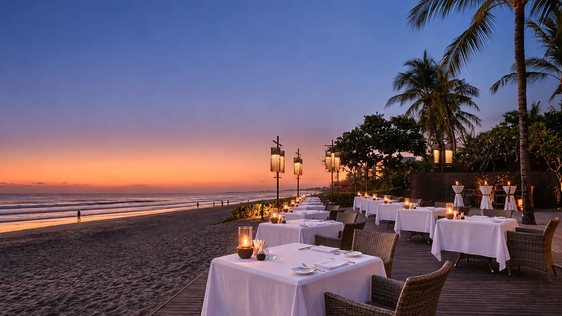 Beachfront restaurant tables on the sand in Seminyak at sunset, with lanterns and palms