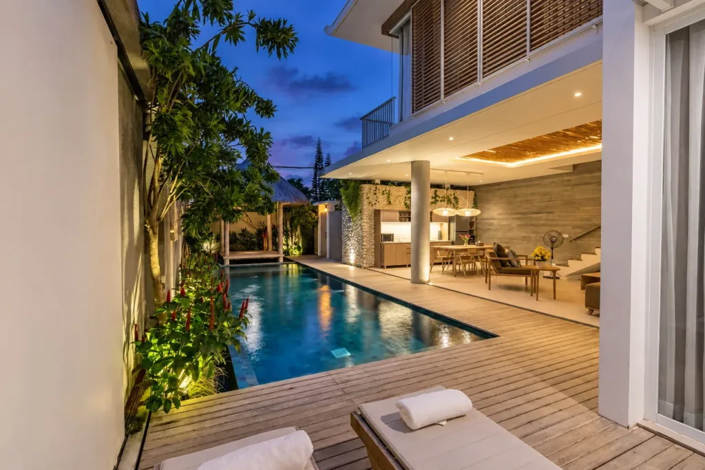 Villa Swan 02 — pool, lit at dusk with two sun loungers in the foreground and the living room glowing behind
