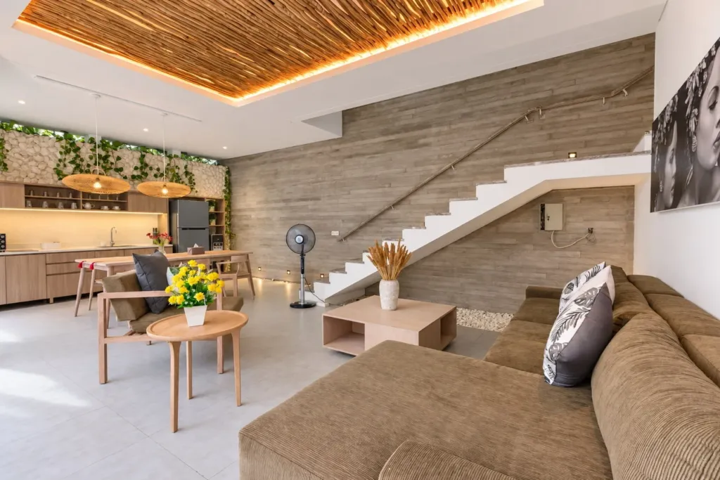 Villa Swan 02 — living, sectional sofa and open timber staircase under a thatched ceiling
