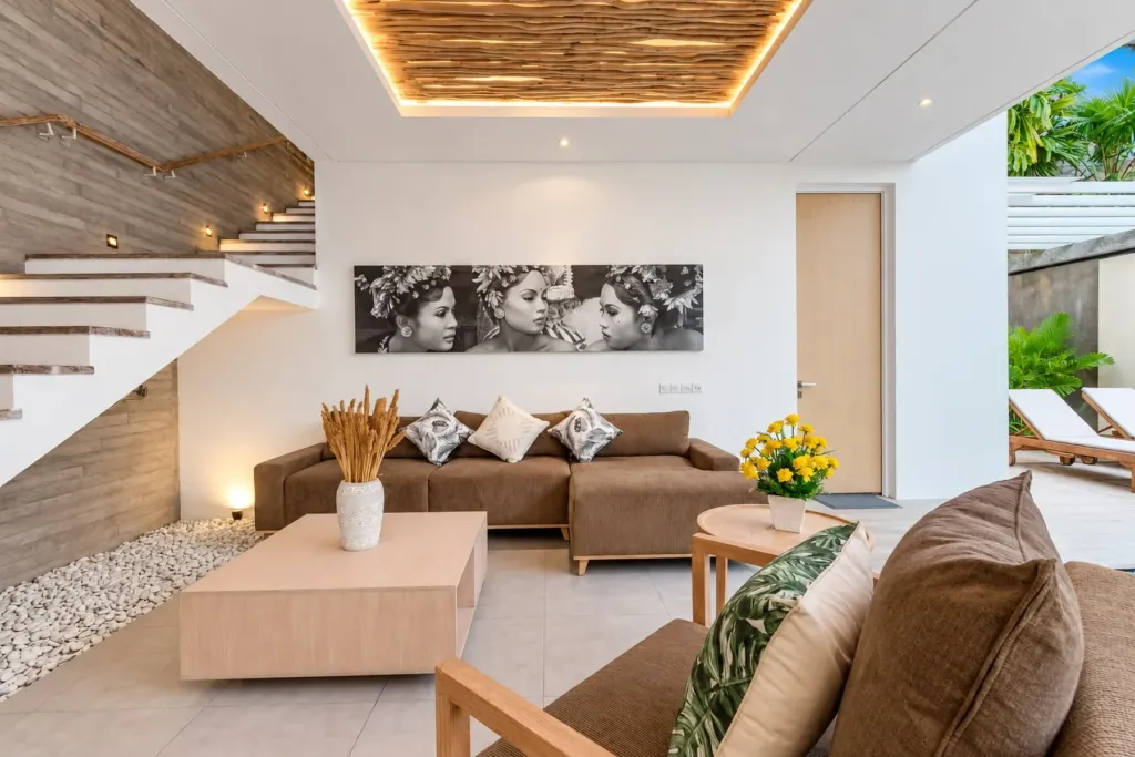 Villa Swan 02 — living, deep brown sectional, timber staircase and a black-and-white Balinese portrait canvas