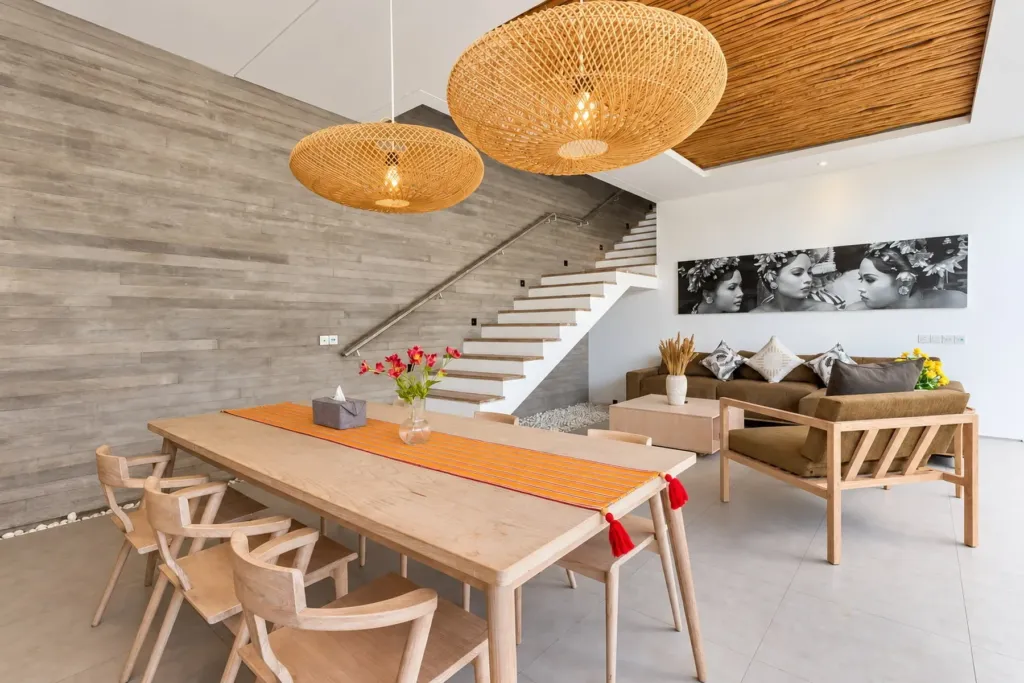 Villa Swan 02 — dining, timber table under two rattan pendants with the sofa and staircase behind