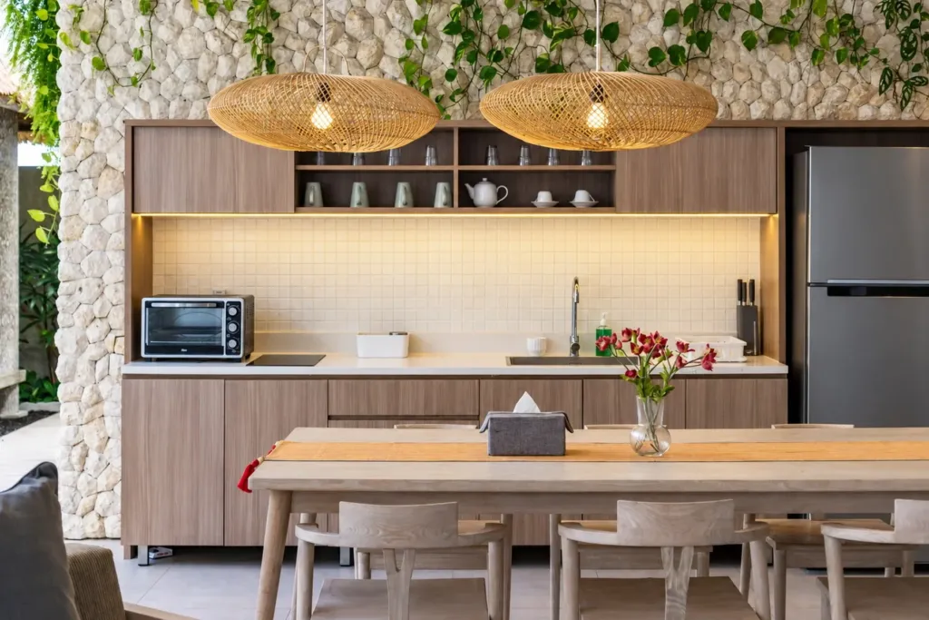 Villa Swan 02 — kitchen, timber cabinetry, open shelving and two woven rattan pendants against stacked stone