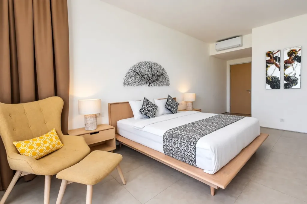 Villa Swan 02 — bedroom 1, king bed, mustard armchair and footstool under air conditioning
