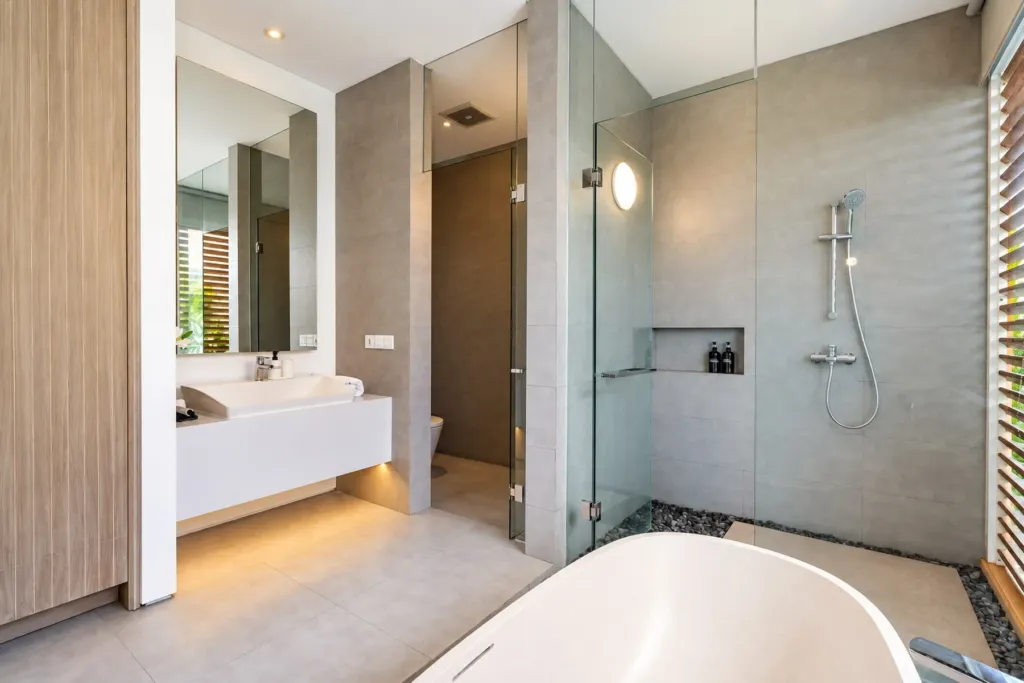 Villa Swan 02 — bathroom 1, glass-walled rain shower next to the freestanding bathtub and a stone vanity