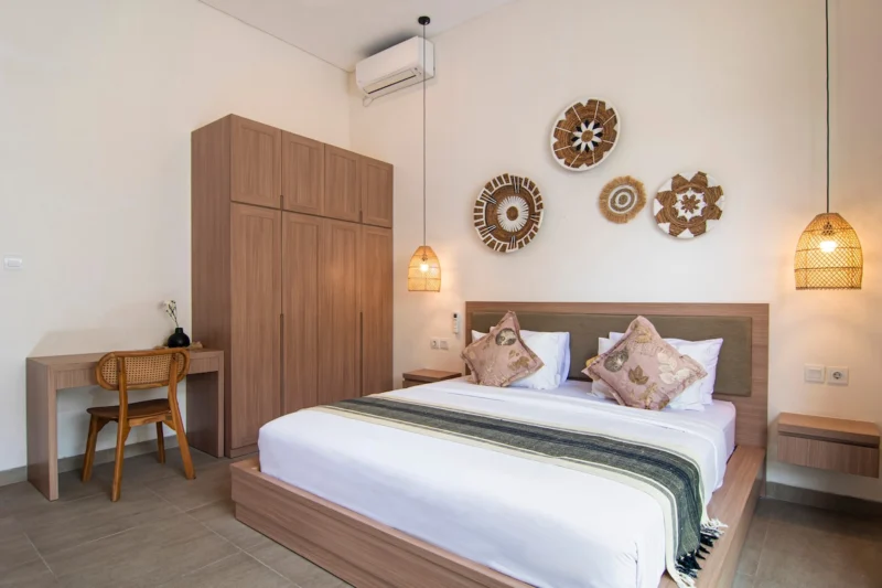Villa LaBumbak, Umalas — bedroom 2, king bed with tall timber wardrobe, desk and cane chair, woven wall discs above the bed