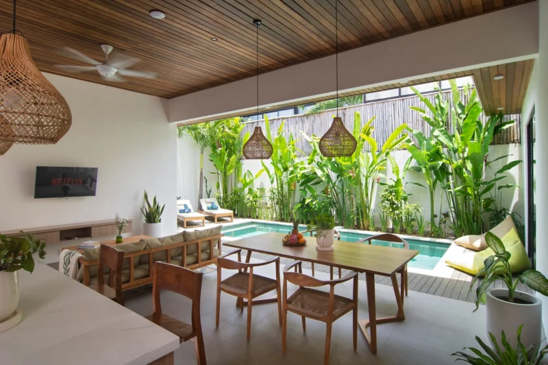 Villa LaBumbak, Umalas — dining, timber dining table under a dark timber ceiling with rattan pendants, open to the pool and dense tropical planting