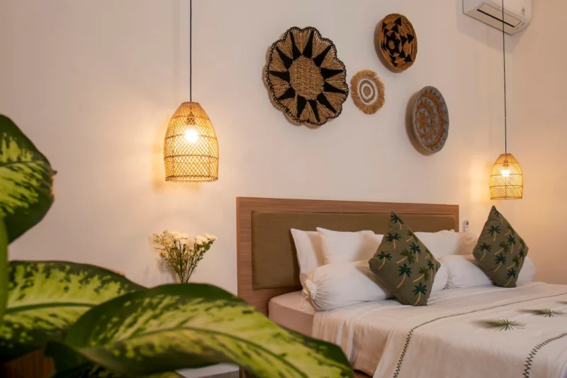 Villa LaBumbak, Umalas — bedroom 1, king bed with palm-print cushions and woven wall discs, foliage in the foreground