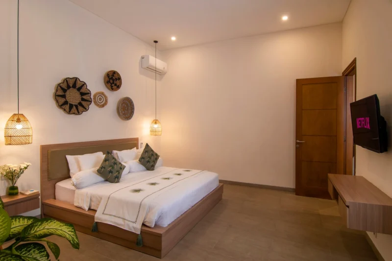 Villa LaBumbak, Umalas — bedroom 1, king bed with palm-print cushions, wall TV and woven discs, timber door to the hallway