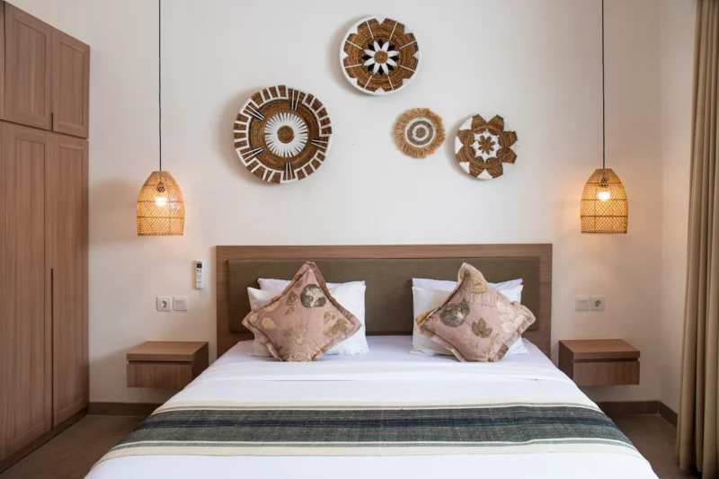 Villa LaBumbak, Umalas — bedroom 2, king bed under a cluster of woven wall discs, rattan pendants either side, wardrobe alongside