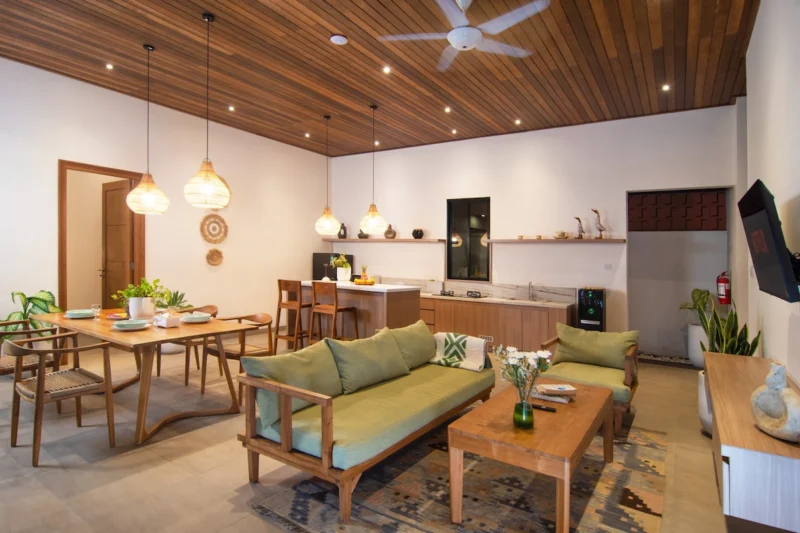 Villa LaBumbak, Umalas — living, teak sofa and coffee table on a patterned rug, dining table and kitchen behind under a dark timber ceiling
