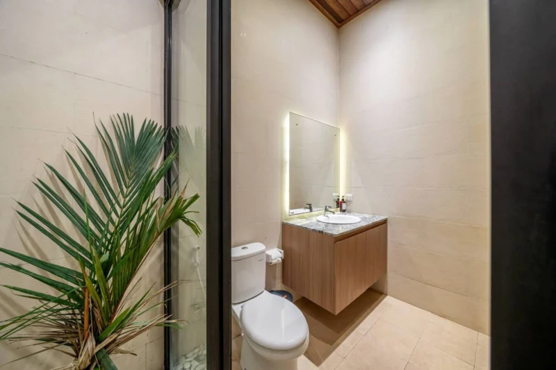 Villa LaBumbak, Umalas — bathroom 1, marble-topped vanity and backlit mirror, palm growing behind the glass screen, timber slat ceiling