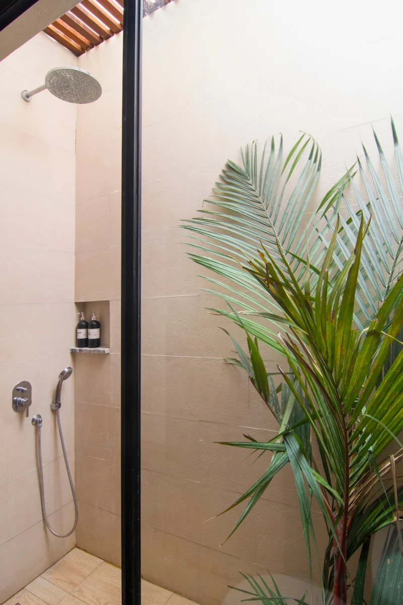 Villa LaBumbak, Umalas — bathroom 1, rain shower and handheld behind black-framed glass, palm planted against the stone wall