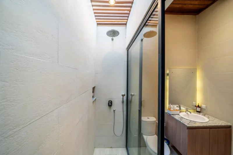 Villa LaBumbak, Umalas — bathroom 2, narrow rain shower behind glass, marble-topped vanity and mirror, timber slat ceiling