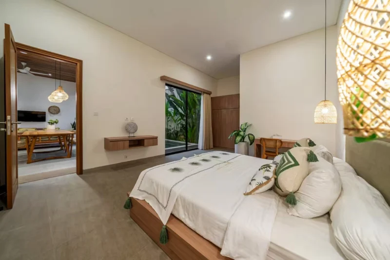 Villa LaBumbak, Umalas — bedroom 1, king bed with green-tasselled linen, doorway through to the dining room, woven pendant alongside