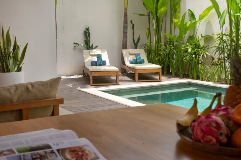 Villa LaBumbak, Umalas — pool, sunloungers beside the pool against a wall of heliconia and palms, bowl of tropical fruit on the timber table in the foreground